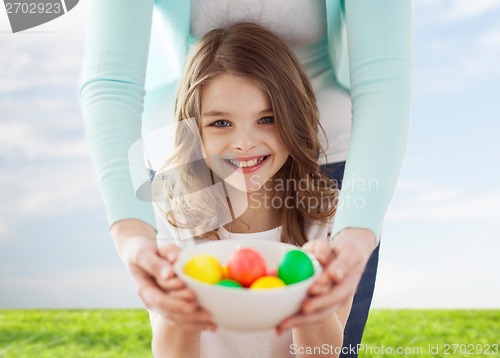 Image of smiling girl and mother holding colored eggs