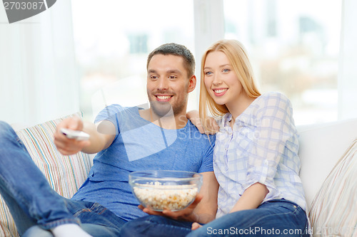 Image of smiling couple with popcorn watching movie at home