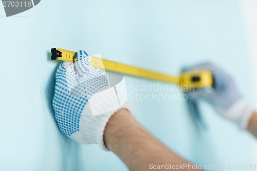 Image of closeup of male in gloves measuring wall with tape