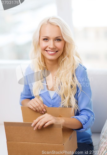 Image of smiling young woman opening cardboard box at home