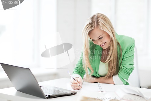 Image of smiling student girl writing in notebook