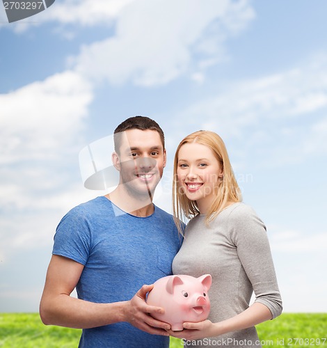 Image of smiling couple holding big piggy bank