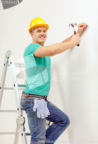 Image of smiling man in helmet hammering nail in wall