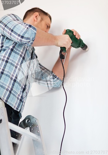 Image of man with electric drill making hole in wall