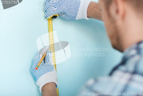 Image of closeup of male in gloves measuring wall with tape