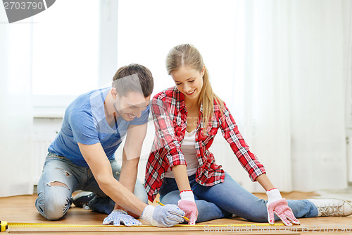 Image of smiling couple measuring wood flooring