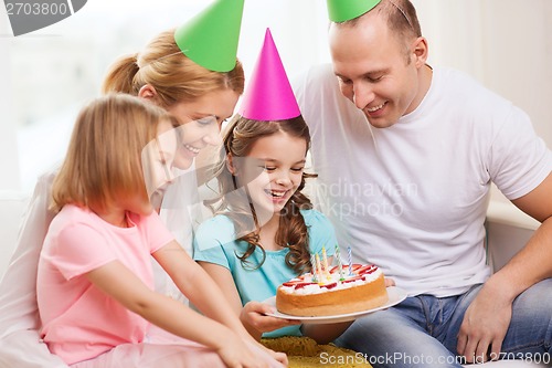 Image of smiling family with two kids in hats with cake