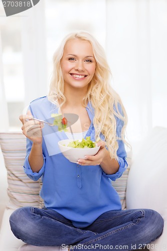 Image of smiling young woman with green salad at home