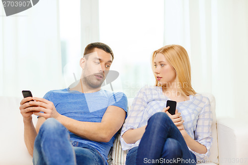 Image of concentrated couple with smartphones at home