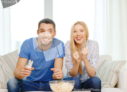 Image of smiling couple with popcorn cheering sports team