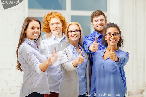 Image of happy creative team showing thumbs up in office