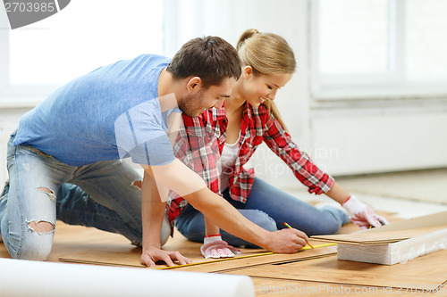 Image of smiling couple measuring wood flooring