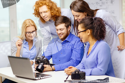 Image of smiling team with laptop and photocamera in office