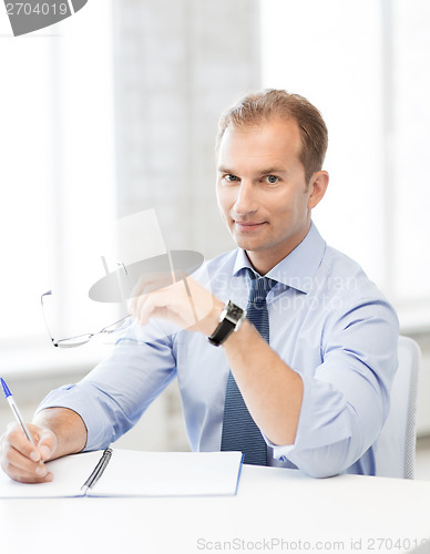 Image of businessman with spectacles writing in notebook