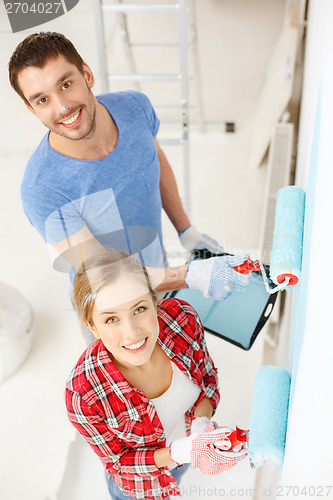 Image of smiling couple painting wall at home