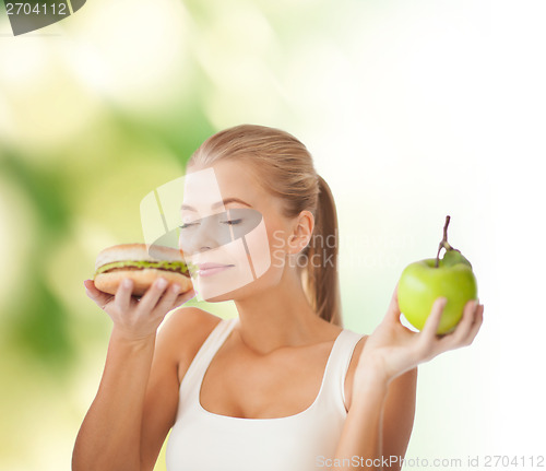 Image of woman smelling hamburger and holding apple