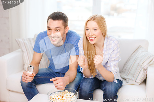 Image of smiling couple with popcorn cheering sports team