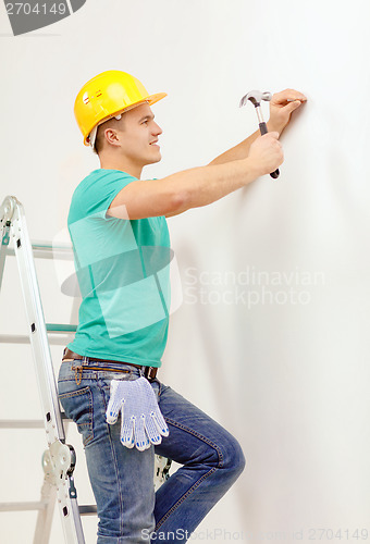 Image of smiling man in helmet hammering nail in wall