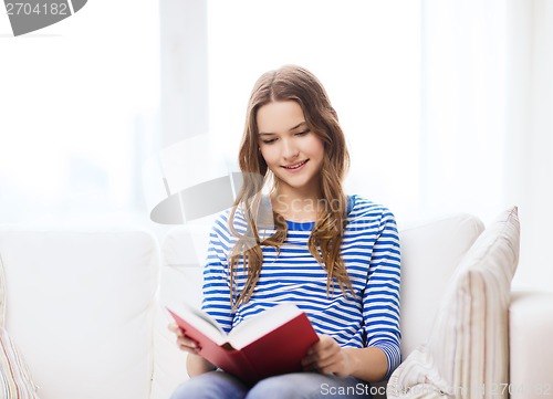 Image of smiling teenage girl reading book on couch