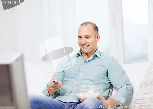 Image of smiling man with popcorn watching movie at home