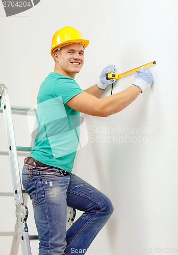 Image of smiling man in protective helmet measuring wall