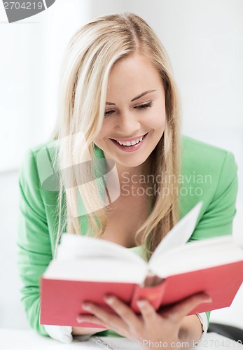 Image of smiling young woman reading book at school