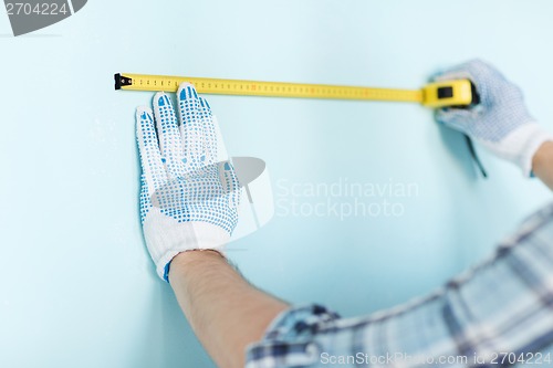 Image of closeup of male in gloves measuring wall with tape