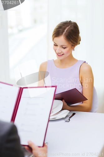 Image of smiling young woman looking at menu at restaurant