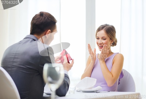 Image of excited young woman looking at boyfriend with box