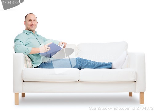 Image of smiling man lying on sofa with book