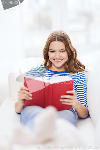 Image of smiling teenage girl reading book on couch