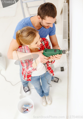 Image of smiling couple drilling hole in wall at home