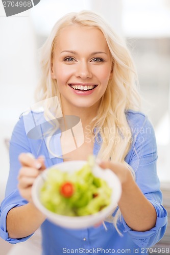 Image of smiling young woman with green salad at home