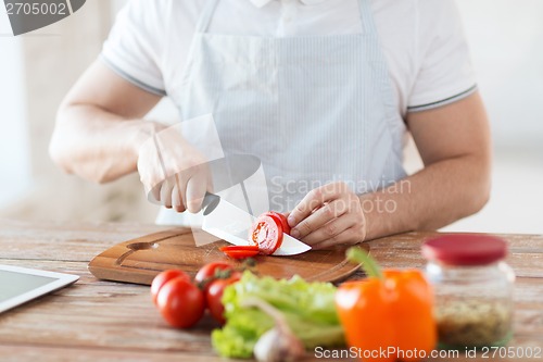 Image of male hand cutting tomato on board with knife