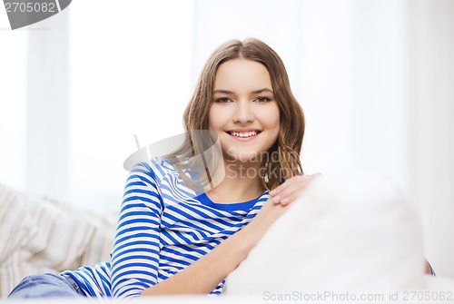 Image of smiling teenage girl sitting on sofa at home