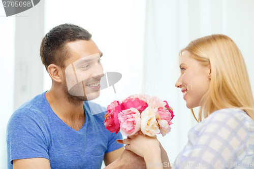 Image of smiling man giving girfriens flowers at home