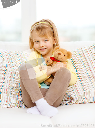 Image of smiling girl with teddy bear sitting on sofa