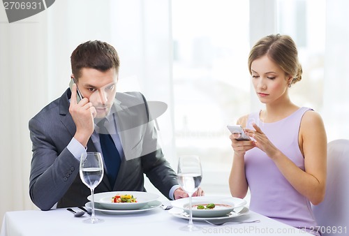 Image of busy couple with smartphones at restaurant