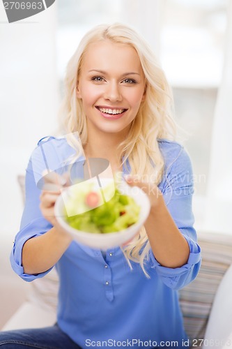 Image of smiling young woman with green salad at home