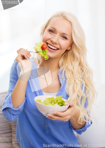 Image of smiling young woman with green salad at home