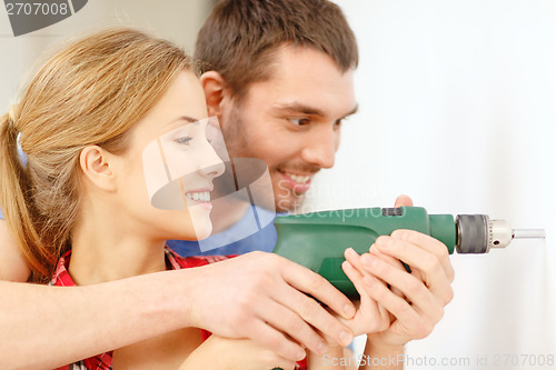 Image of smiling couple drilling hole in wall at home