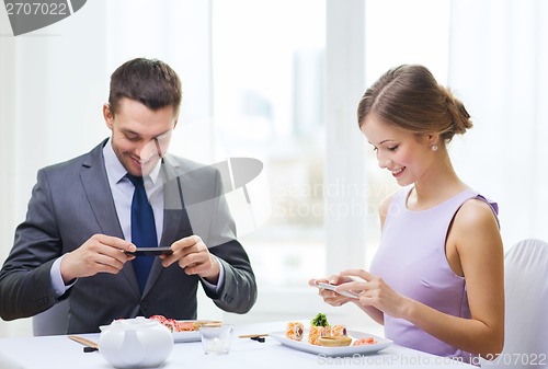 Image of smiling couple with sushi and smartphones