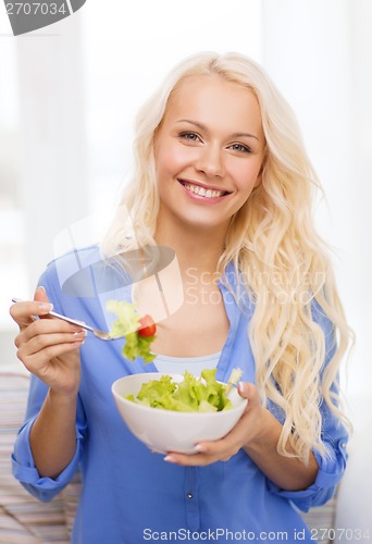 Image of smiling young woman with green salad at home