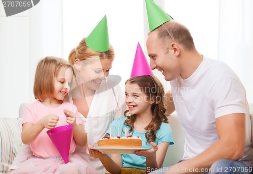 Image of smiling family with two kids in hats with cake