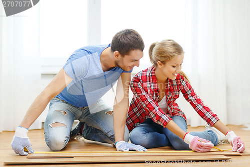 Image of smiling couple measuring wood flooring