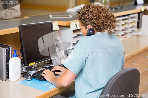 Image of Nurse Answering Telephone While Working On Computer At Reception