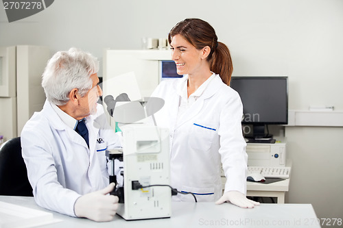 Image of Scientist Discussing With Colleague While Using Microscope
