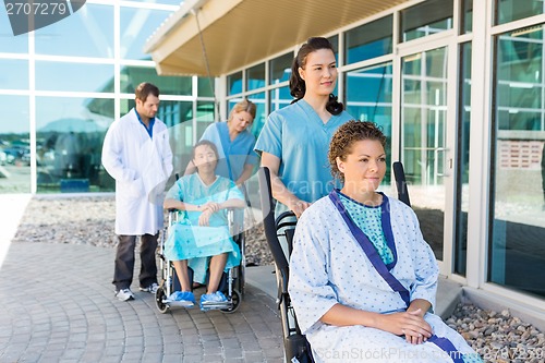 Image of Nurses Assisting Patients On Wheelchairs Outside Hospital Buildi