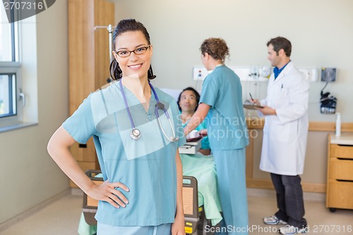 Image of Nurse With Hand On Hip Against Patient And Medical Team