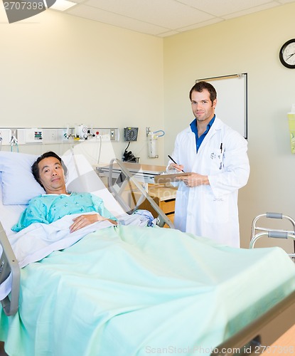 Image of Doctor Writing On Clipboard By Patient's Bed In Hospital